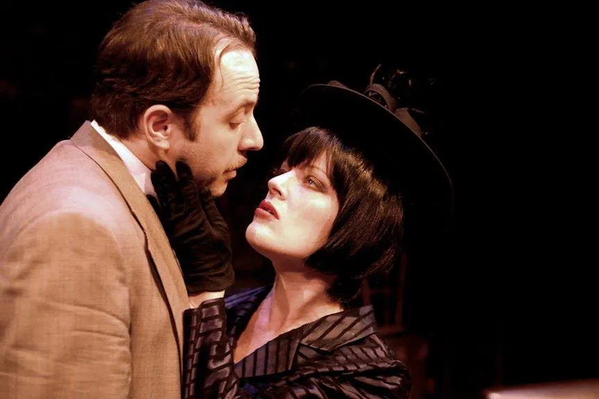 A woman with black hair is wearing a hat looking at a man standing next to her.
A woman dressed as a vampire looks up at a man beside her.