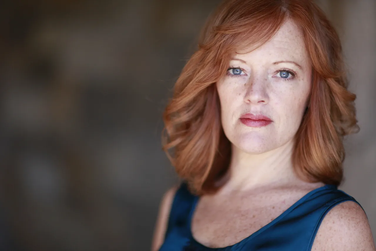 A woman wearing a blue top stands with her arms crossed.