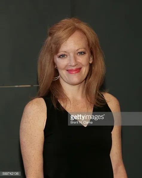 A lady with long brown hair dressed in a black top is posing for a picture.