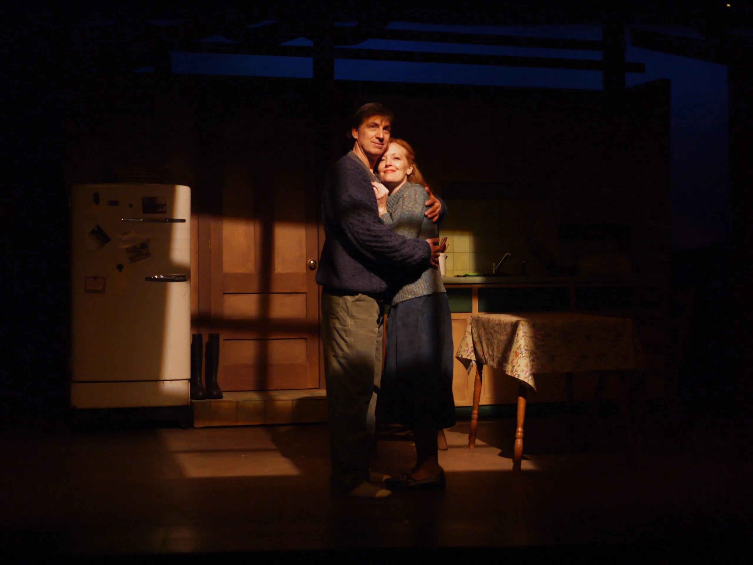 A man hugging a woman with another person behind them on the stage.
A man embracing a woman, with another person standing close by.
Two people are hugged on stage, with one person in between.