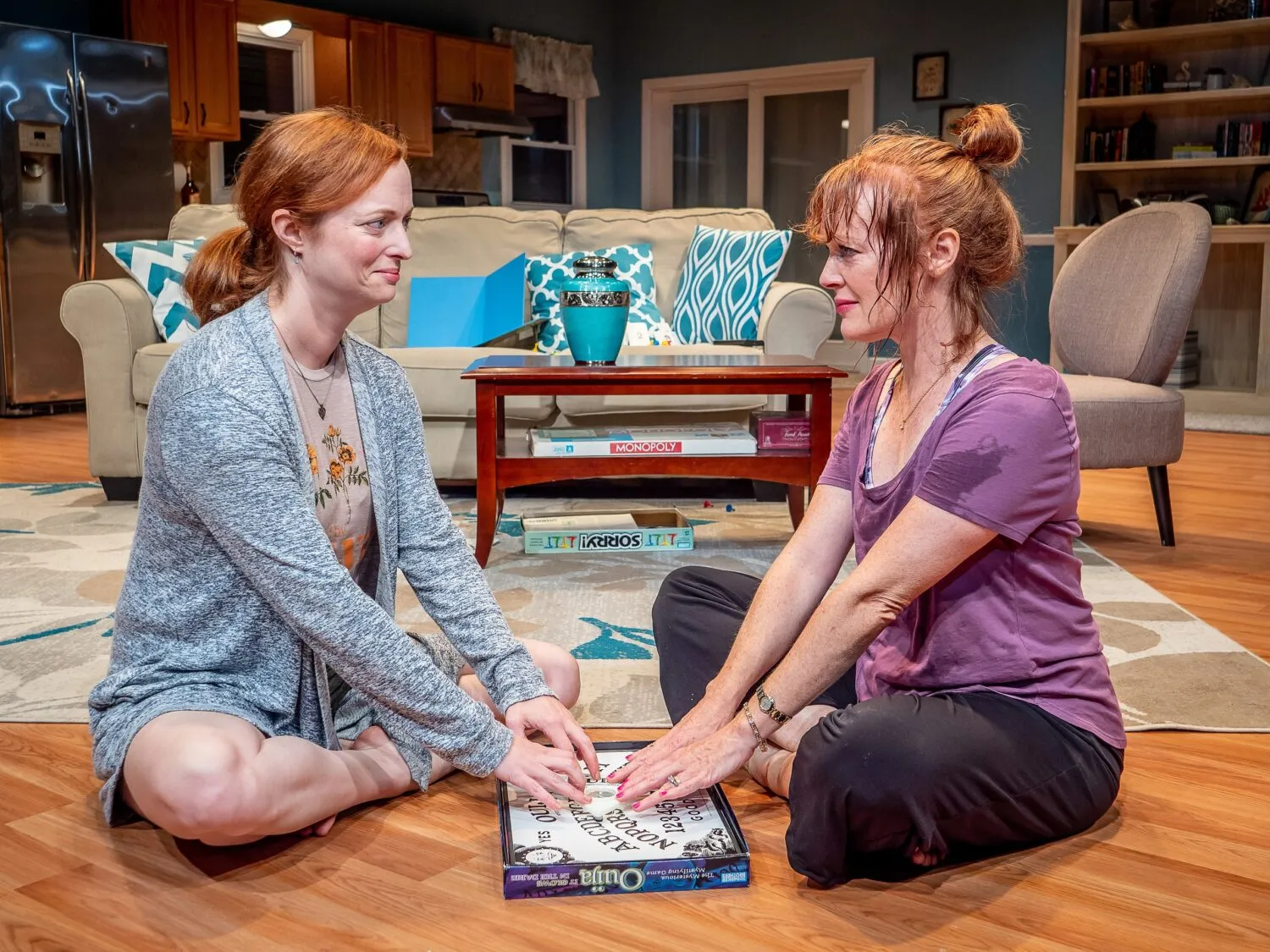 Two women sitting on the floor playing a game with a board that has letters on it.