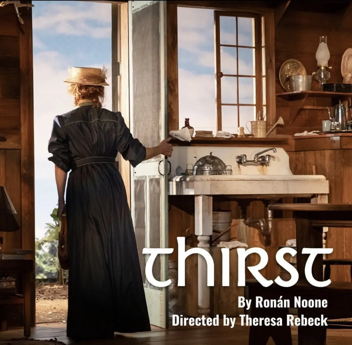 A woman dressed in a long blue dress with a hat stands in an open door by a sink.